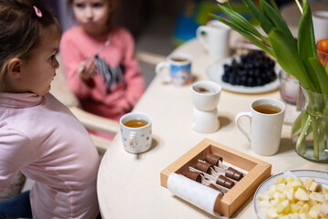 Children eat fruits and desserts, drink tea at home in the evening kitchen. Chocolate on a stick for melting.