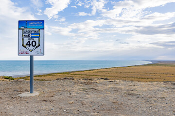 View to the coast of Cabo Virgenes and aluminum sign marking kilometer 0 of the famous Ruta40 in...