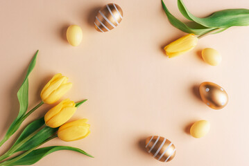 Obraz na płótnie Canvas Frame of golden and yellow decorated easter eggs and tulips on neutral beige background. Top view, flat lay, copy space