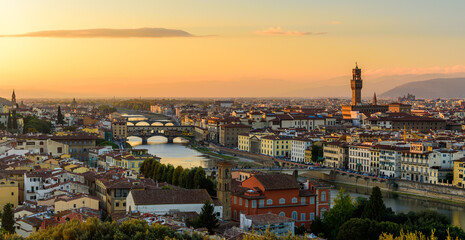 The Florence cityscape with the Ponte Vecchio over Arno river and Palazzo Vecchio in an orange sunset.
