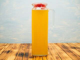 Orange juice in a jug. Glass jug with orange juice on a wooden table on a blue background.