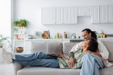 Positive african american couple using laptop while sitting on couch at home.