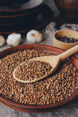 Raw buckwheat in earthenware with wooden spoon in a rustic setting.