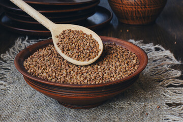 Raw buckwheat in earthenware with wooden spoon in a rustic setting. Side view.