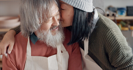 Pottery, creative and senior couple talking about art with hug and kiss together in a studio class. Elderly Asian man and woman hugging with love while learning and working with clay on a date - Powered by Adobe