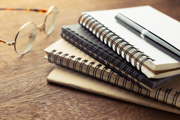 Spiral small notebook pile with pen and eyeglasses on the wood desk, category short note, create writing job, education, tips for content writing