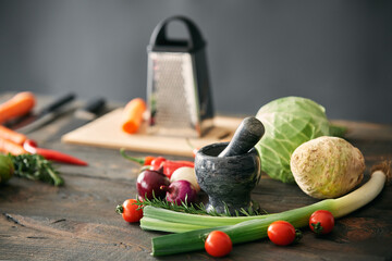Background with assorted raw organic vegetables and black marble mortar with a pestle on wooden...