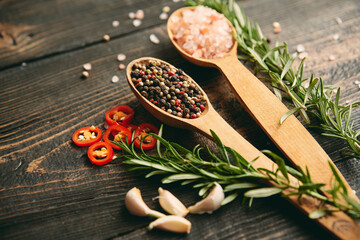 Close up photo of mixed peppercorns and sea salt in wooden spoons, fresh rosemary and garlic on...