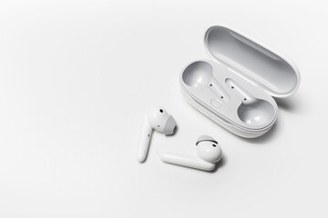Close-up of modern wireless earphones lying near opened charging case on white background with copy...