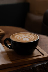 Black cup of cappuccino with latte art on wooden background