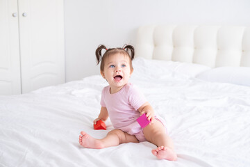 funny baby girl in pink bodysuit playing with children wooden cubes toys on bed