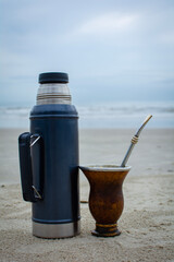 copa de mate con sorbete o bombilla de alpaca y termo de acero sobre la arena, bebiendo un mate en la playa frente al mar, bebida tipica argentina, uruguaya, paraguaya y sur de brasil. © Daniel