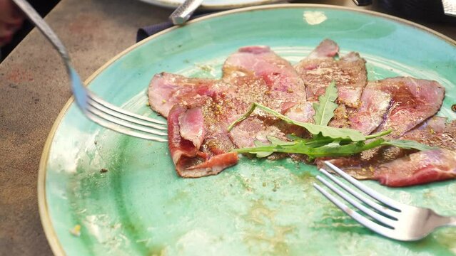 Close up of person skewering pieces of carpaccio with fork from a dish at a restaurant