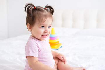 portrait of smiling baby girl in pink bodysuit with 2 tails on bed