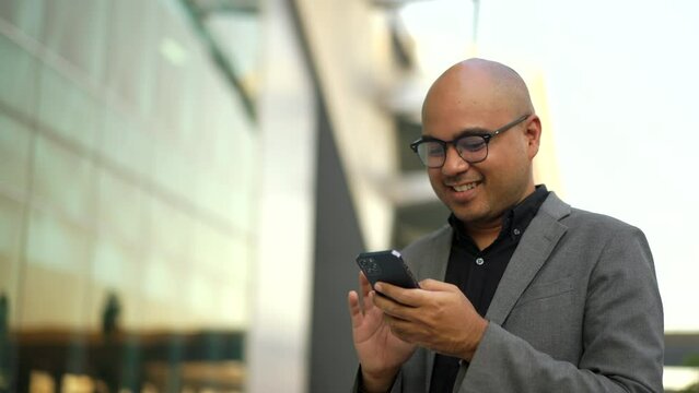 Confident smartly businessman manager smiling and using smartphone in a modern office. CEO, business owner check balance from mobile phone proud of his success goals. Portrait Middle eastern trader.