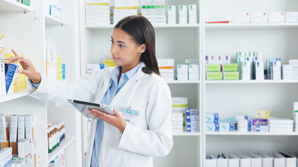 A young female pharmacist stocktaking in a dispensary using a tablet. Doctor preparing...