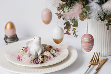 Banner. The concept of a bright Easter holiday. A bouquet of flowers with feathers, white rabbits and Easter eggs in a plate on a white isolated background. Beautiful Easter card.