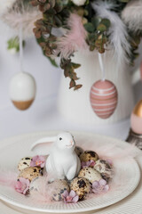 Banner. The concept of a bright Easter holiday. A bouquet of flowers with feathers, white rabbits and Easter eggs in a plate on a white isolated background. Beautiful Easter card.