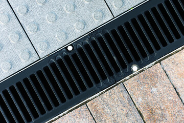 Cast iron storm sewer grate on a marble walkway. Close-up