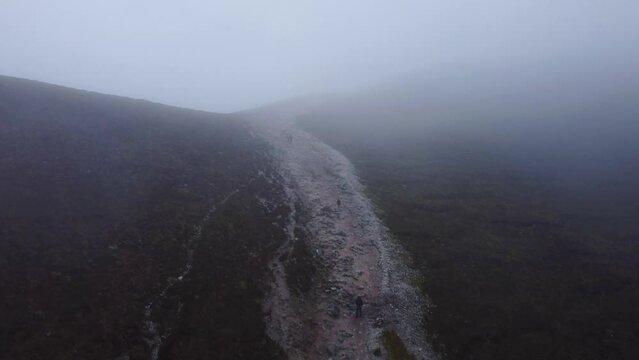 Rising aerial shot of people descending Irish mountain trail in the fog