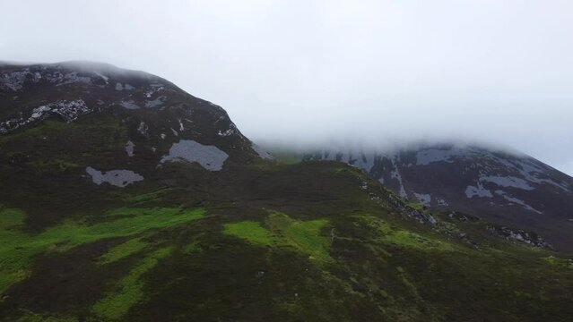 Tracking aerial shot of Irish mountain summit covered in fog