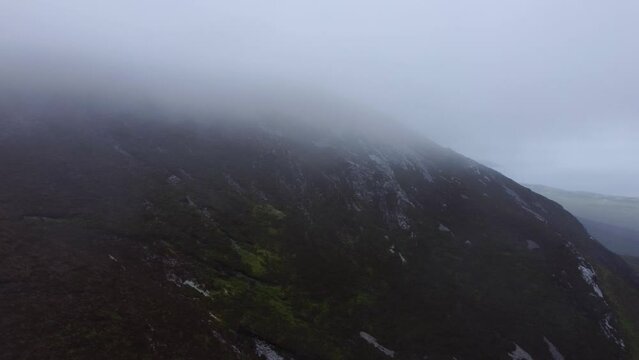 Aerial tracking shot of fog rolling over Irish mountain