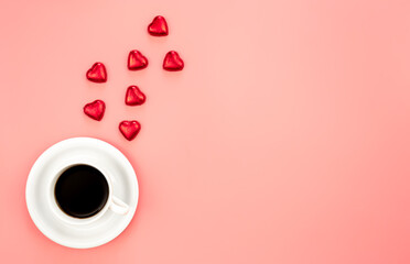 Cup of coffee and heart shaped sweets on a pink background, flat lay.