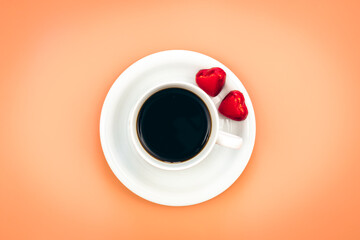 Cup of coffee and heart shaped candies on orange background, flat lay.