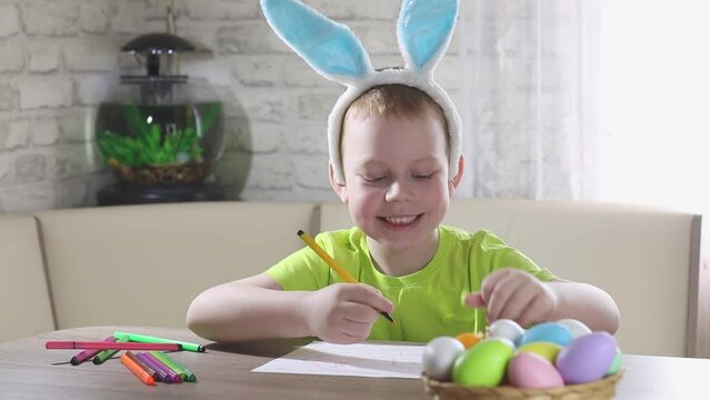 Easter kids. A happy boy with rabbit ears on his head smiles, plays at home with colored eggs and draws. Preparing for Easters the Big Egg Hunt. Easter Bunny. Easter eggs.