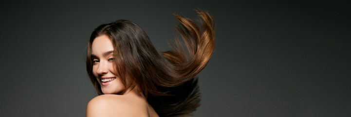 Fototapeta premium Portrait of beautiful young girl with silk long brunette hair posing over grey studio background. Taking care after hair. Concept of natural beauty, youth, skincare, cosmetology, cosmetics