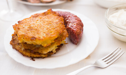 Potato pancakes with fried sausage on white plate