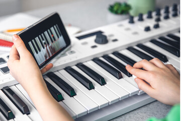 Plakat The child learns to play the piano with a smartphone, online music lesson.