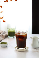 A cup of cold black coffee and a cup of matcha tea in the afternoon sun on a table. Sunny breakfast atmosphere. Popular food and drink trend.
Iced coffee and green matcha on a light blurred background