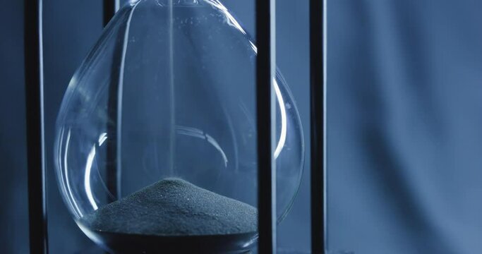 Closeup of sand timer clock with sand flowing from through hourglass on blue tone., Follow focus
