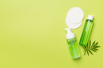 Foaming facial cleanser and micellar water on color background, top view