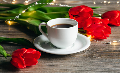 Fototapeta na wymiar Cup of coffee and red tulips on a wooden surface.