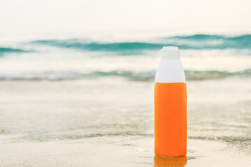 Sunscreen spray in orange bottle on the sand against the backdrop of sea waves. The concept of applying sunscreen during a beach holiday. Layout for adding text, banner, blank for design.