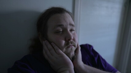 One pensive overweight suffering from anxiety sitting at home in the dark. Close up face of a preoccupied male person