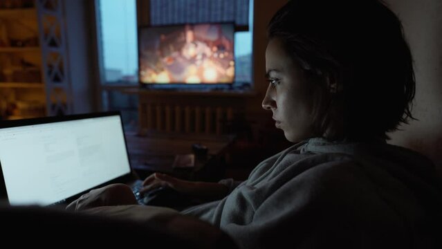 woman sits in dark room at home on couch with laptop, working remotely, shopping online. freelancer, remate work, workplace at home