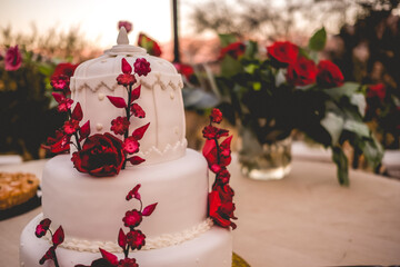 Beautiful white wedding cake with red roses and flowers made of sugar decoration in a wedding table at sunset