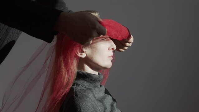 Portrait of a woman in profile. The face is brightly lit. A man covers a woman's eyes with a red bandage. Violence in family. Criminal offense. Psychological trauma. Sexual undertones.