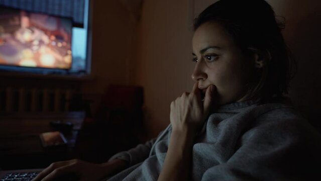 woman sits in dark room at home on couch with laptop, working remotely, shopping online. freelancer, remate work, workplace at home