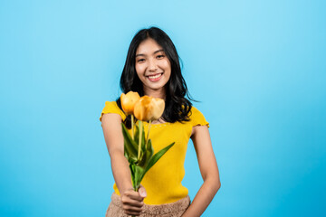 portrait, long haired girl wearing shirt yellow tights, She held bouquet yellow lilies in his hand, With shy look, and smiling happily, looking at camera, Isolated indoor studio on blue background.