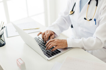 Doctor typing on a laptop in her office, accessing patient records on an EHR software