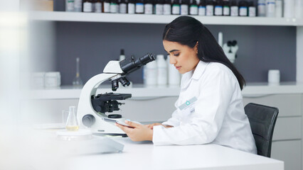 Young scientist using a digital tablet and microscope in a lab. Female pathologist analyzing...