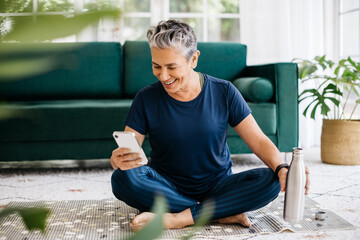 Happy senior woman using a smartphone during yoga, tracking her fitness progress on a smart app - obrazy, fototapety, plakaty