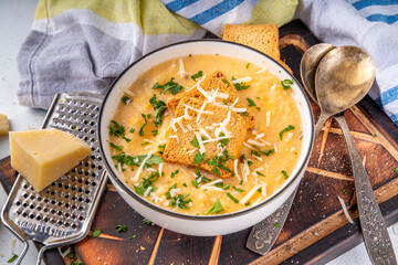 Homemade cheese cream soup, cheddar parmesan soup with croutons and greens, on white kitchen table...