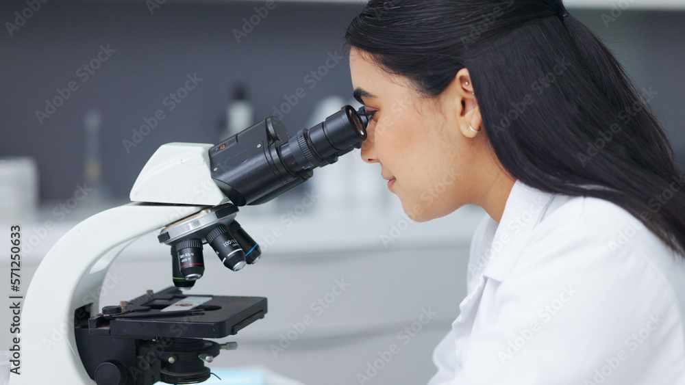Poster Female scientist using a microscope in a research lab. Young biologist or biotechnology researcher working and analyzing microscopic samples with the latest laboratory tech equipment