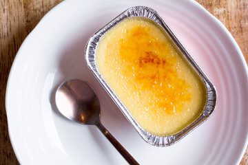 .French Creme Brulee in a foil cup on the white plate, with the spoon on the side.