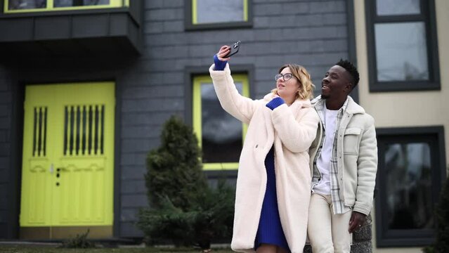 Young interracial couple takes a selfie together on street against background of houses.
